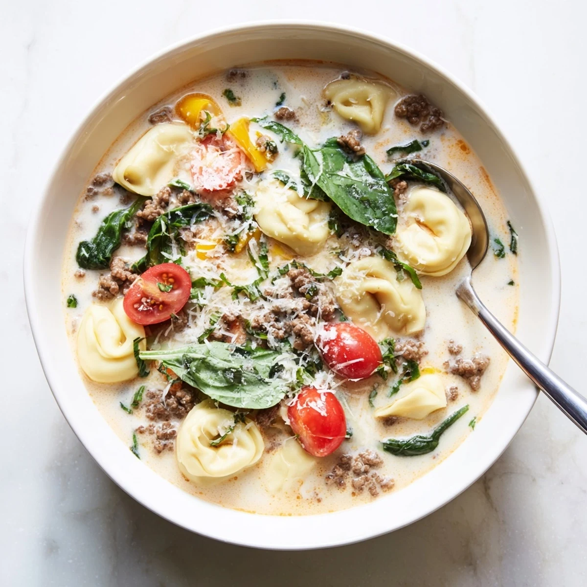 Steaming bowl of homemade Tortellini Beef Soup with savory ground beef and sweet cherry tomatoes in a creamy broth.