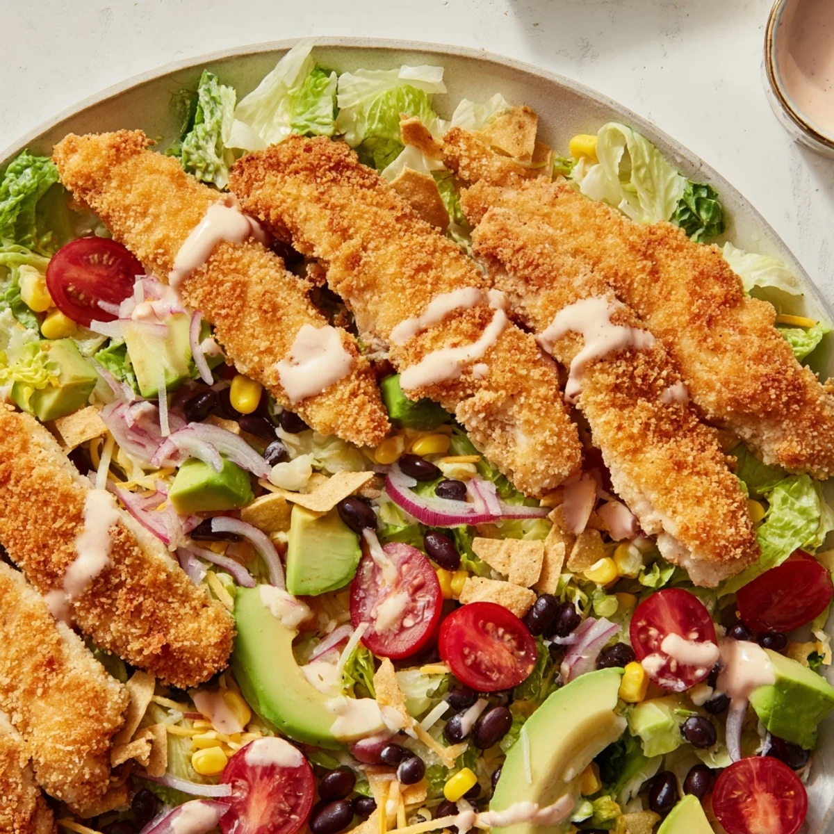 Golden, crunchy chicken strips rest on a bed of crisp romaine, black beans, corn, and cheddar, topped with tortilla strips and creamy salsa ranch.