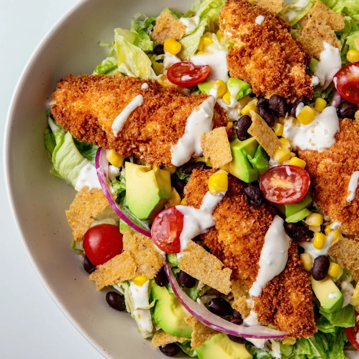 A close-up view of a crispy chicken taco salad, featuring golden-brown chicken strips, fresh chopped romaine lettuce, cherry tomatoes, black beans, and corn.