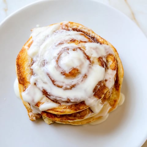 Golden-brown Cinnamon Roll Pancakes drizzled with sweet cream cheese frosting, ready for breakfast.