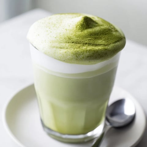 Bright green creamy matcha latte, frothy and inviting, topped with fluffy cold foam, a perfect treat.