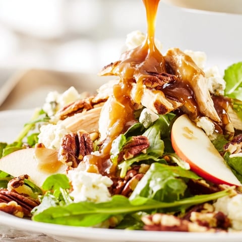 A close-up of Caramel Apple Chicken Salad with sliced Honeycrisp apples, tender chicken, and feta on mixed greens, drizzled with a rich caramel-pecan dressing.