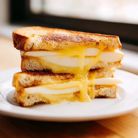 A golden-brown Smoked Gouda & Apple Grilled Cheese sandwich sliced diagonally, revealing melted cheese and crisp apple layers.