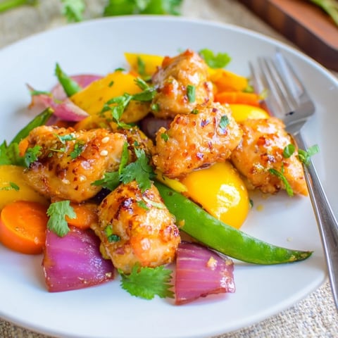 Tender chicken pieces and colorful spring vegetables, glazed in honey garlic sauce, roast on a single sheet pan for an easy weeknight dinner.