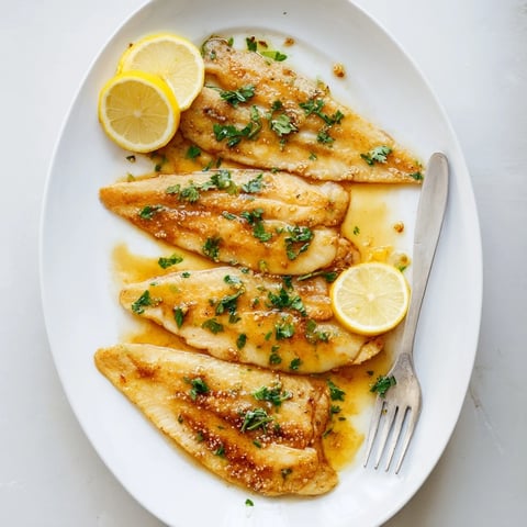 Golden-brown flounder meunière fillets glistening with lemon-browned butter sauce, garnished with fresh parsley.  
