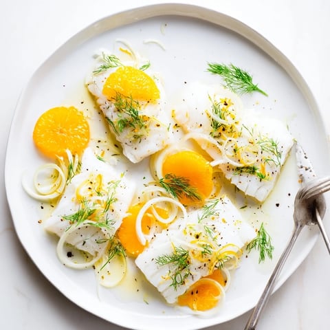 Delicate poached cod fillets nestled with orange slices and fennel fronds in a shallow white bowl.  