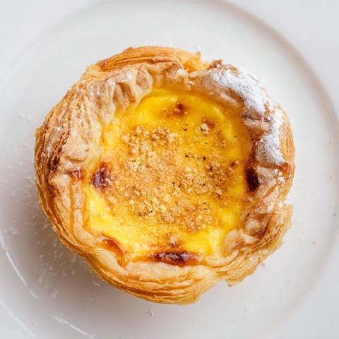 Picture twelve beautifully baked Portuguese egg tarts, nestled in flaky phyllo pastry cups, ready to eat.