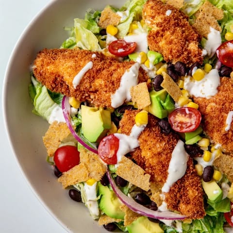 A close-up view of a crispy chicken taco salad, featuring golden-brown chicken strips, fresh chopped romaine lettuce, cherry tomatoes, black beans, and corn.