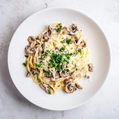 A close-up of velvety mushroom Alfredo pasta, showing golden sautéed mushrooms and grated Parmesan in a rich, creamy sauce.