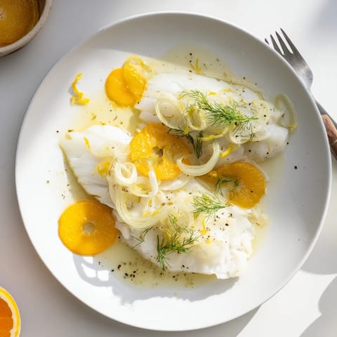 A close-up of Poached Cod With Fennel and Orange, garnished with aromatic herbs and citrus zest.  