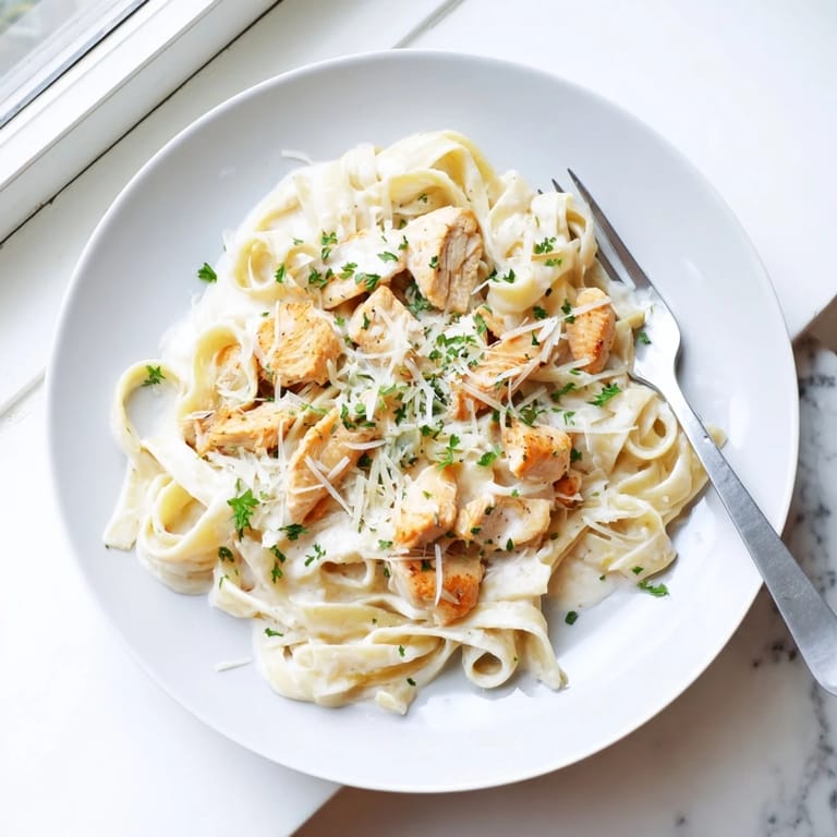 A rustic skillet holds Skillet Chicken Alfredo, featuring savory chicken, creamy sauce, and a sprinkle of Parmesan, ready to serve.