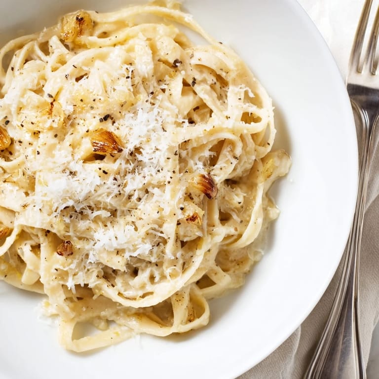 A close-up of roasted garlic cream pasta, highlighting golden, silky sauce clinging to each strand, served warm for a comforting meal.  