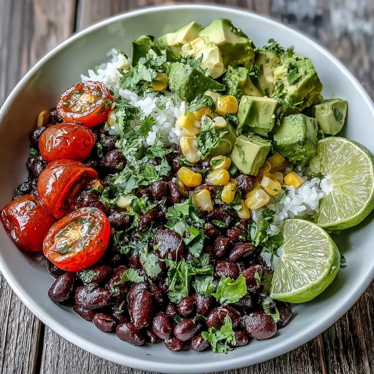 A vibrant Black Bean and Veggie Bowl with black beans, corn, tomatoes, avocado, and lime dressing in a white bowl.