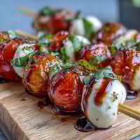 Fresh picnic caprese skewers with juicy cherry tomatoes, creamy mozzarella, and fragrant basil leaves, drizzled with sweet balsamic reduction.