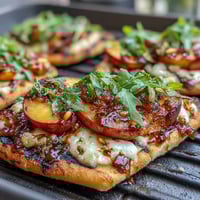 Grilled flatbread topped with sweet peaches, melted Brie, and smoky BBQ sauce, perfect for summer cookouts.  